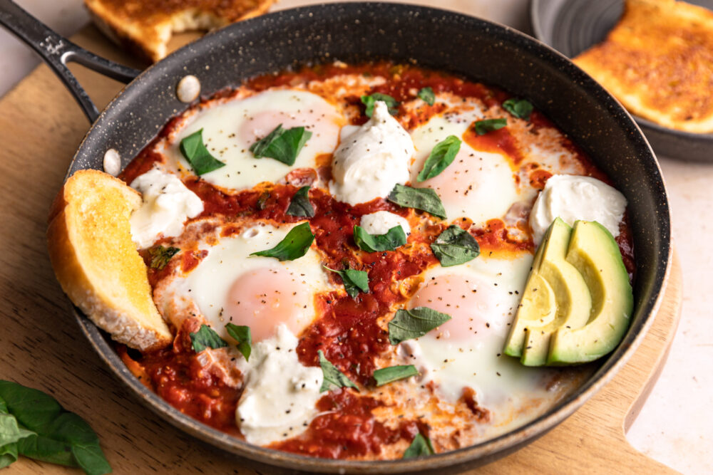 Shakshuka in a dark pan with garnishes and burrata on top.