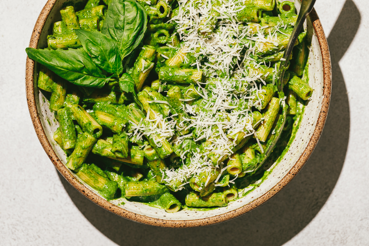 A bowl of green pasta with a spoon and fresh parmesan.