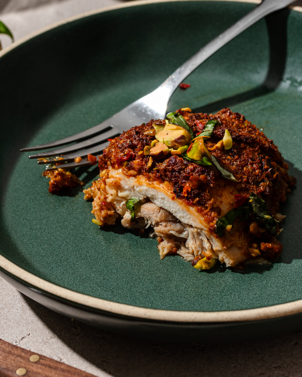 Pistachio crusted chicken on a green plate with a fork.