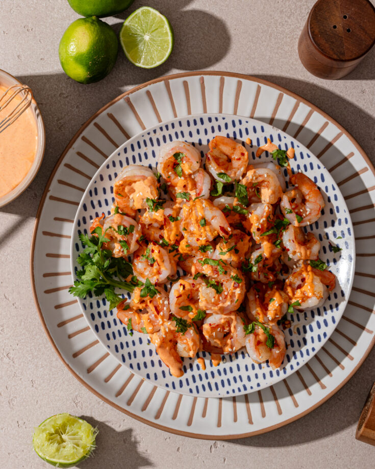 Spicy garlic shrimp on a patterned plate with sauce and toppings.