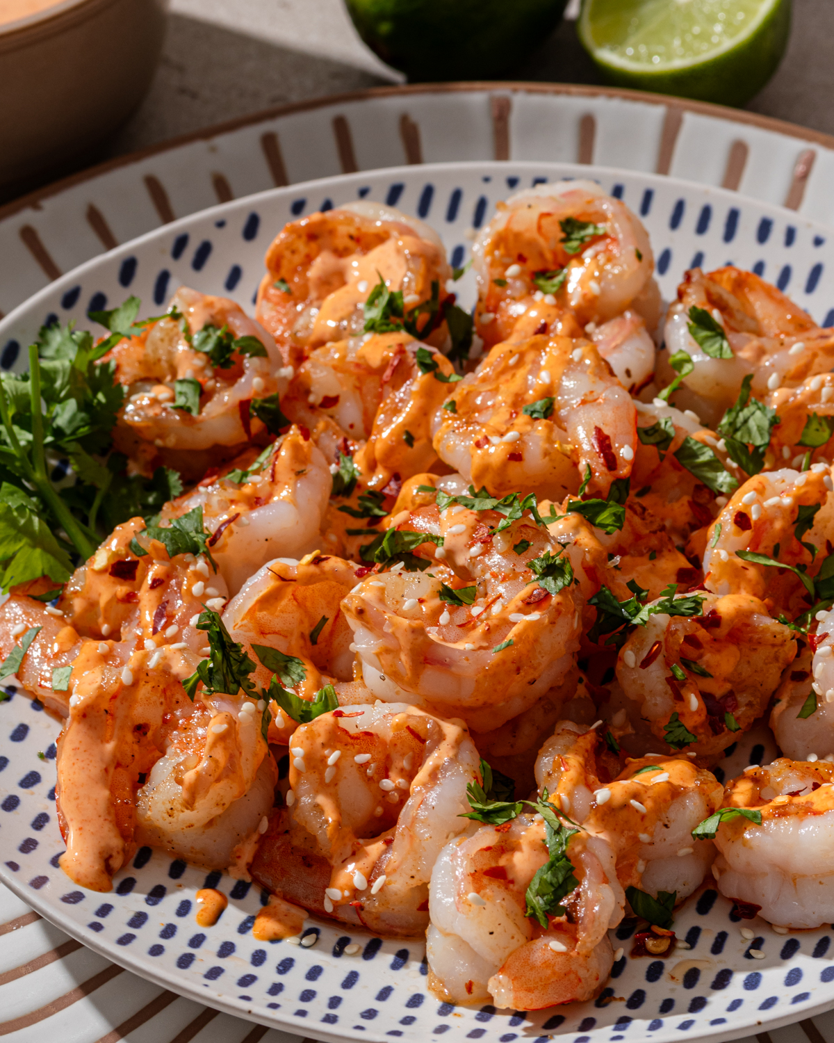 Spicy garlic shrimp on a patterned plate with sauce and toppings.