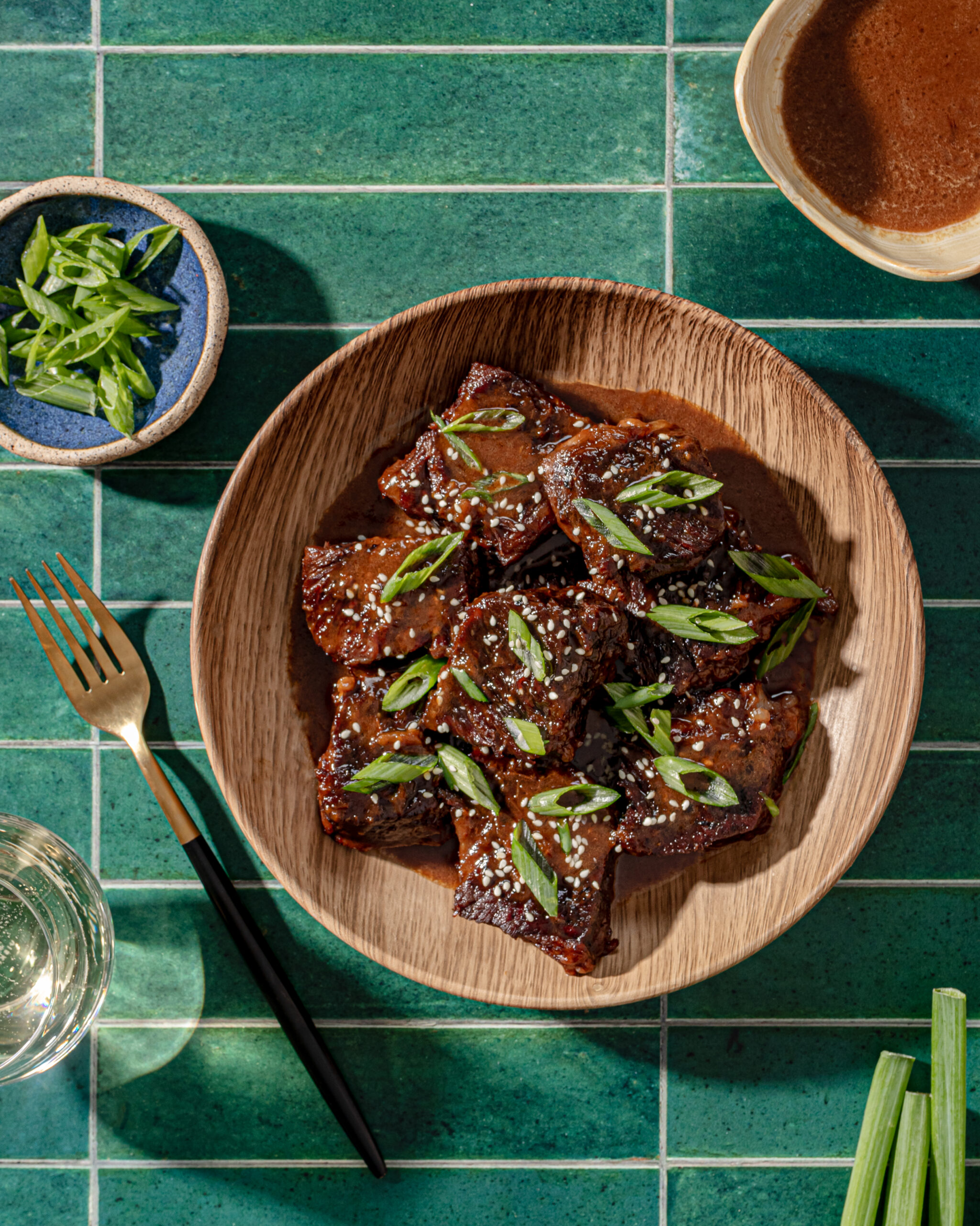 Asian short ribs in a wooden bowl with sauce and garnish.