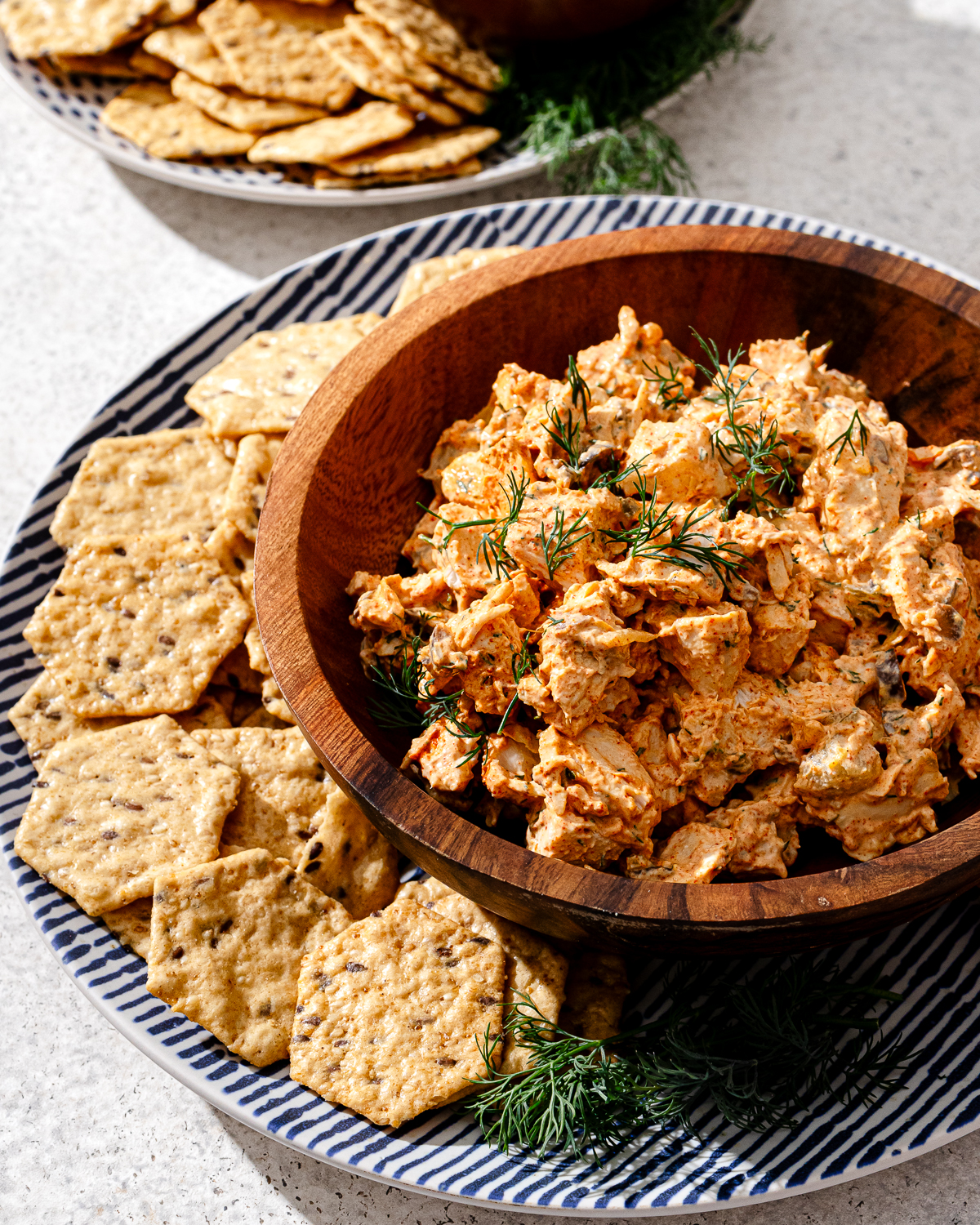 A serving of high protein chicken salad in a wooden bowl with crackers and garnish.