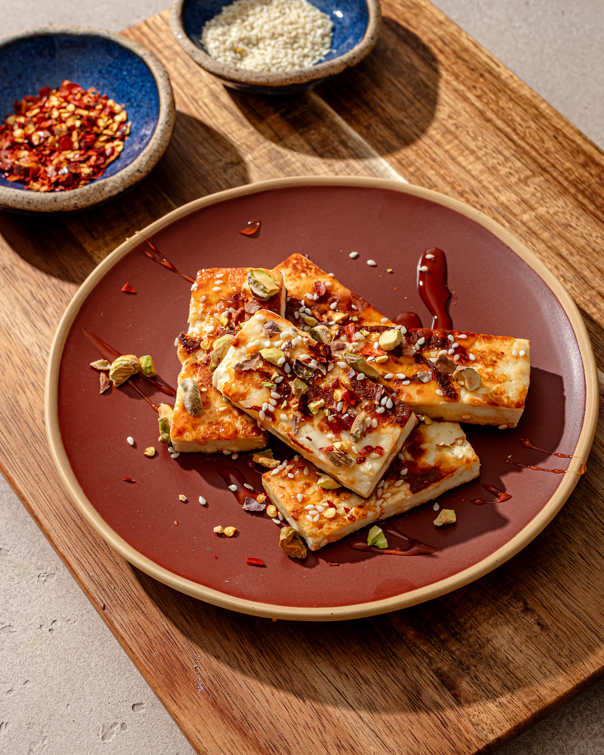A serving of sweet chilli halloumi on a red plate over a wooden cutting board.