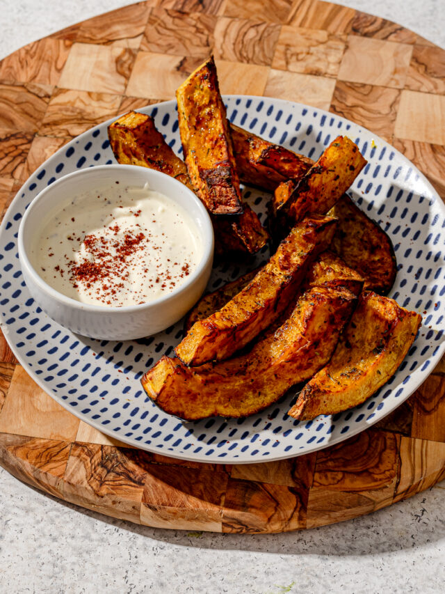 Air fryer acorn squash on a patterned plate with sauce.