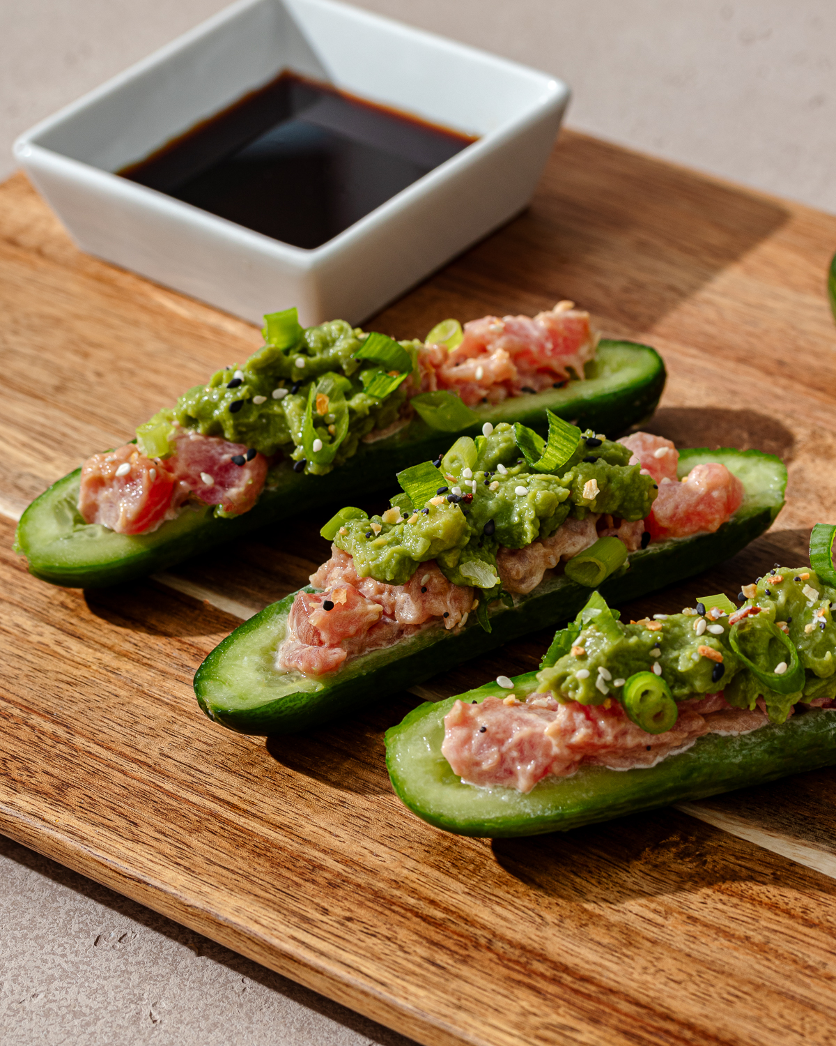 Cucumber sushi boats with sauce and toppings on a wooden cutting board.