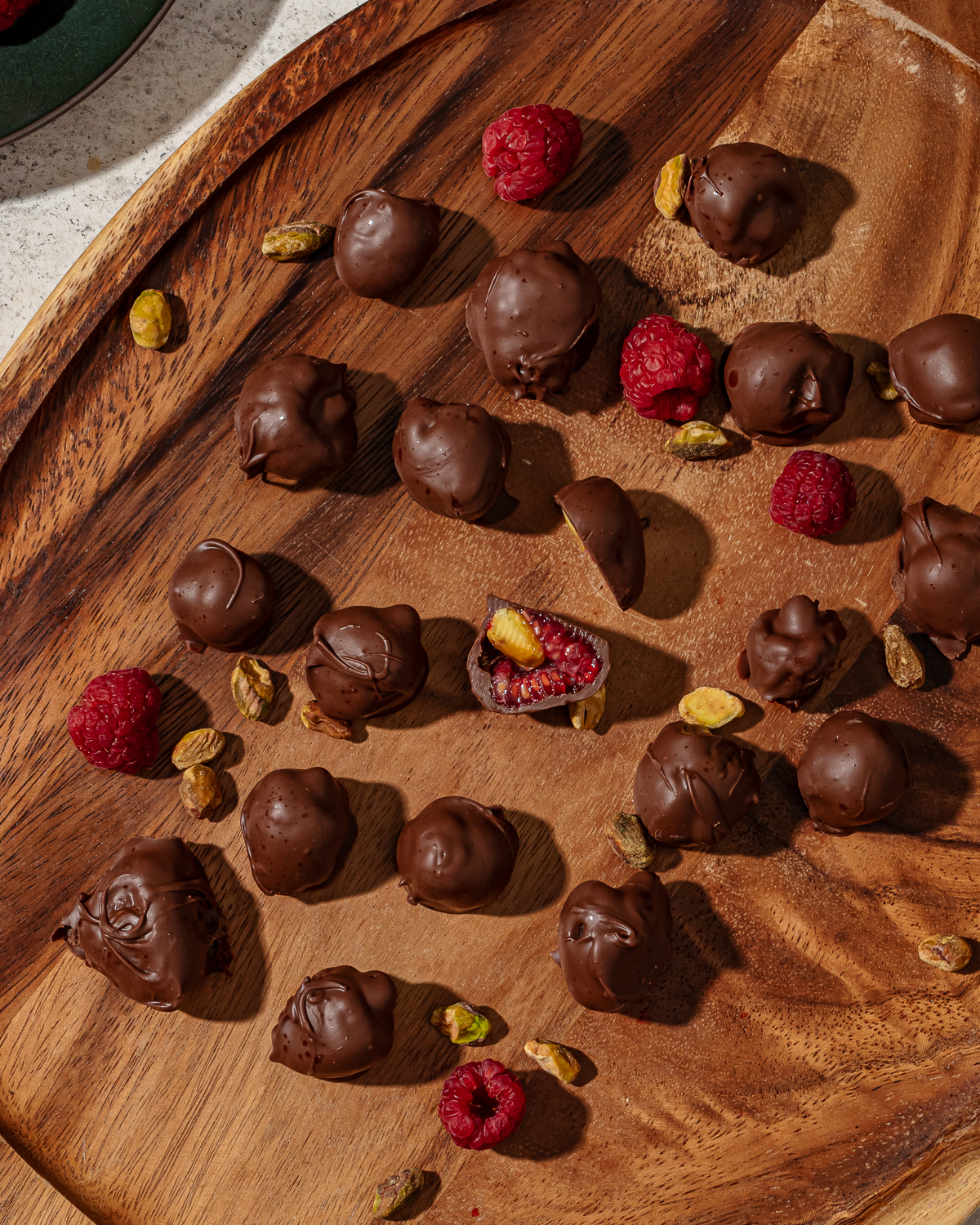 Frozen chocolate covered raspberries on a wooden cutting board.