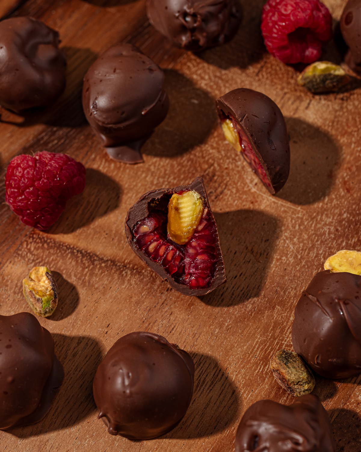 Close up of frozen chocolate covered raspberries on a wooden cutting board.