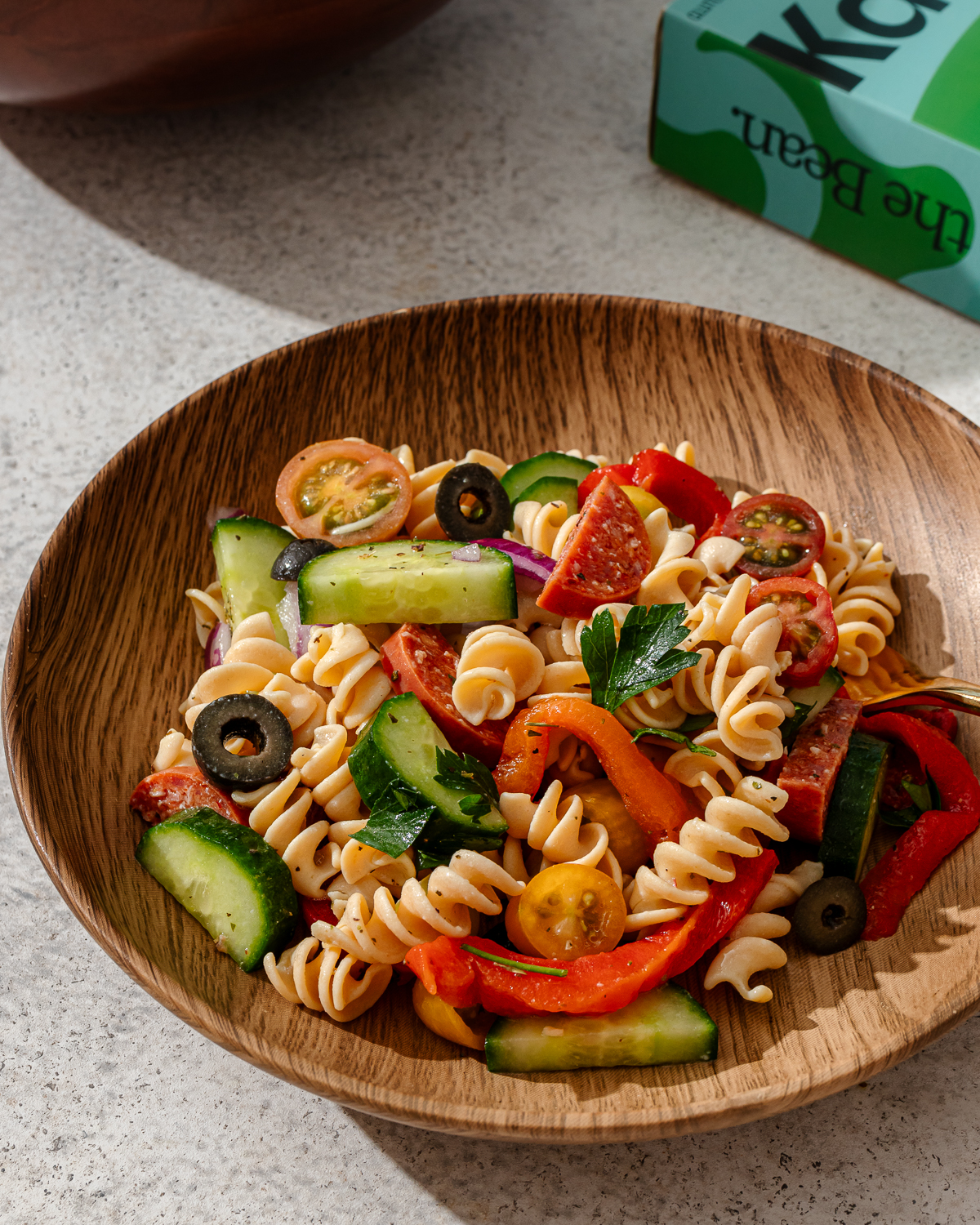 A serving of high protein pasta salad in a wooden bowl over a grape marble surface.
