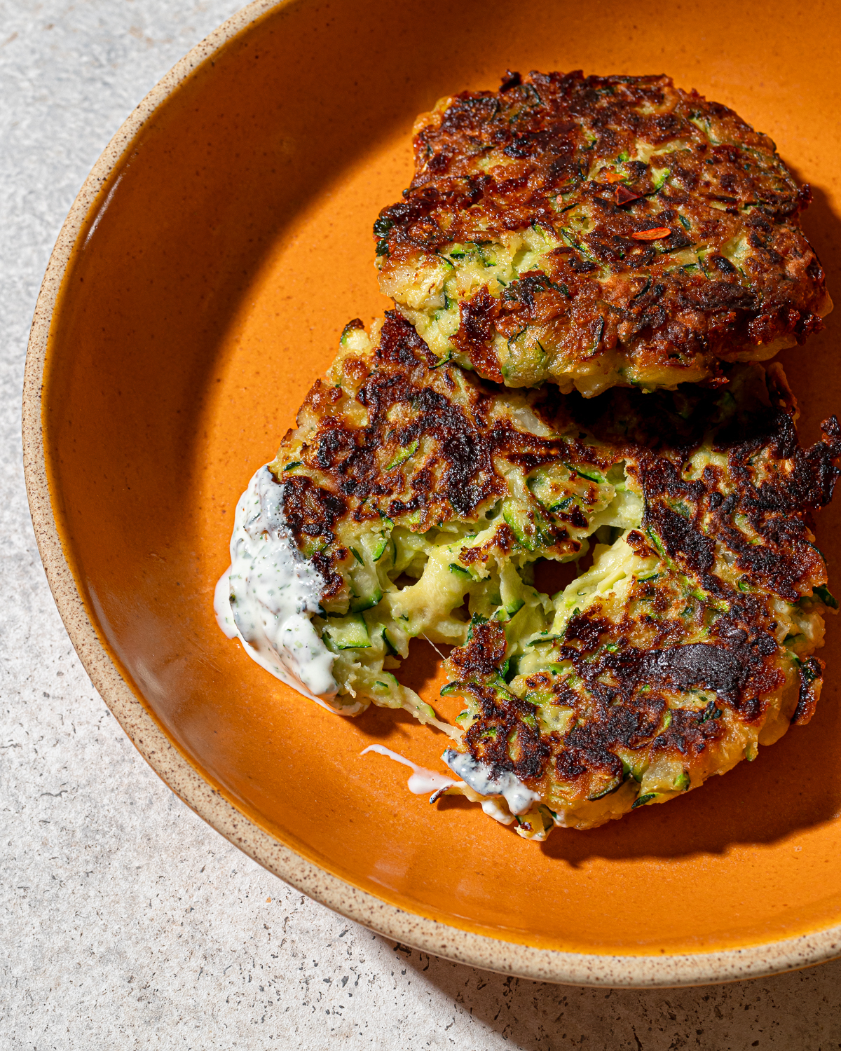 Close-up of zucchini fritters in an orange plate with sauce.