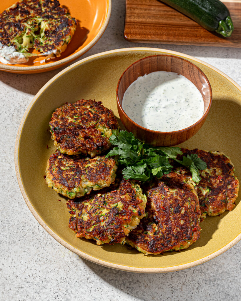 Zucchini fritters in a mustard colored dish with dip.