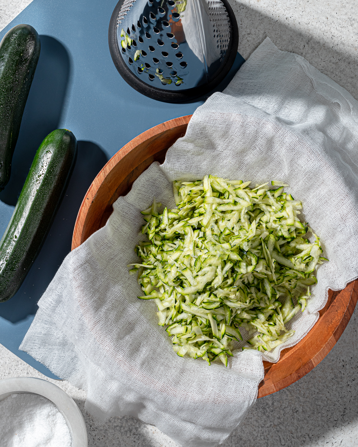 Shredded zucchini in a bowl over a damp paper towel in a bowl.