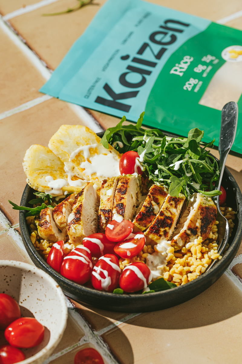 A prepared Mediterranean buddha bowl with a package of Kaizen rice behind it.