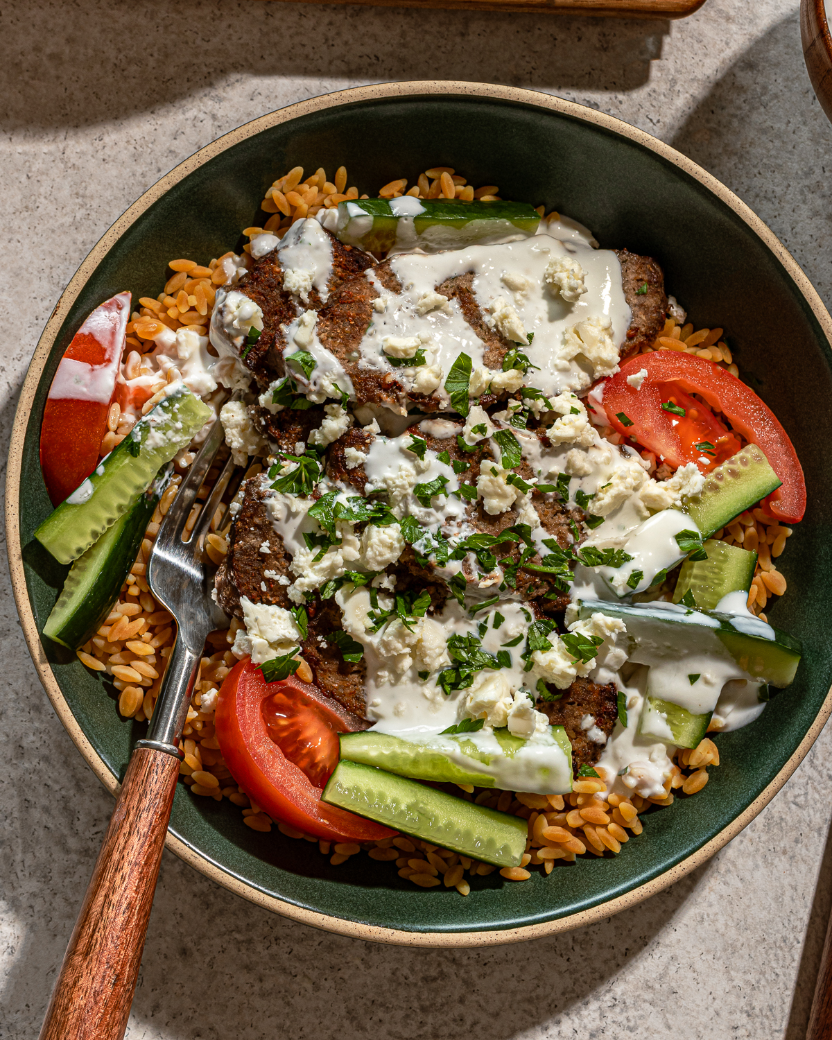 Close up of gyro bowl recipe with fork, sauce, and toppings.