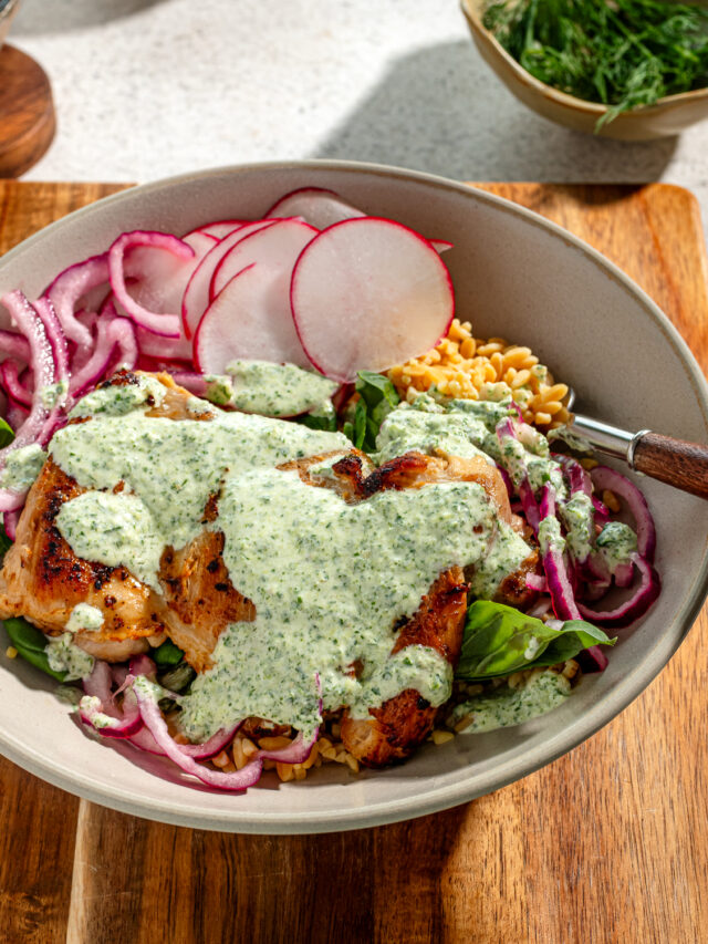 Green goddess chicken thighs in a gray bowl with sauce and toppings over a wooden surface.