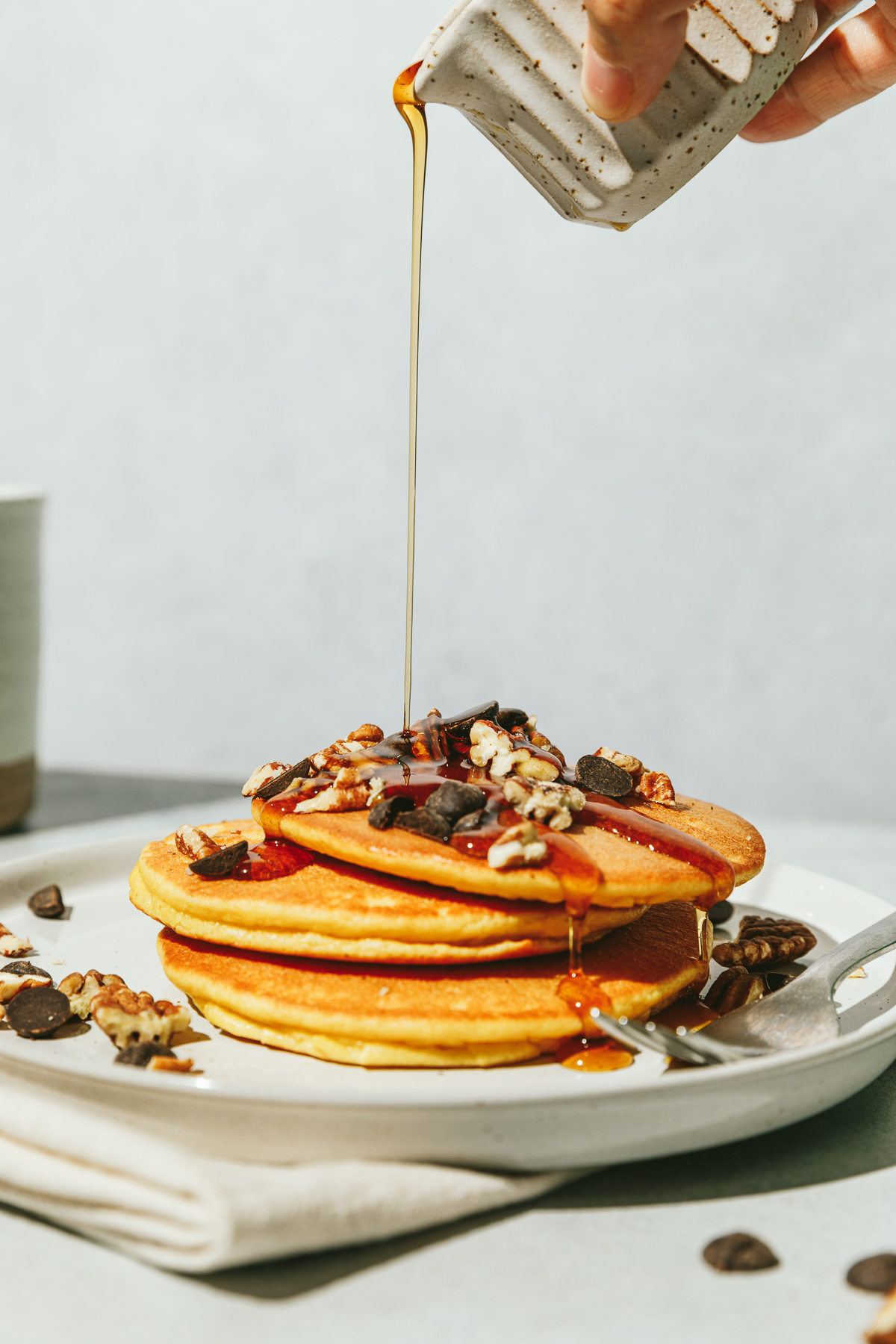 Maple syrup pouring on lupin flour pancakes on a white plate with a gray background.