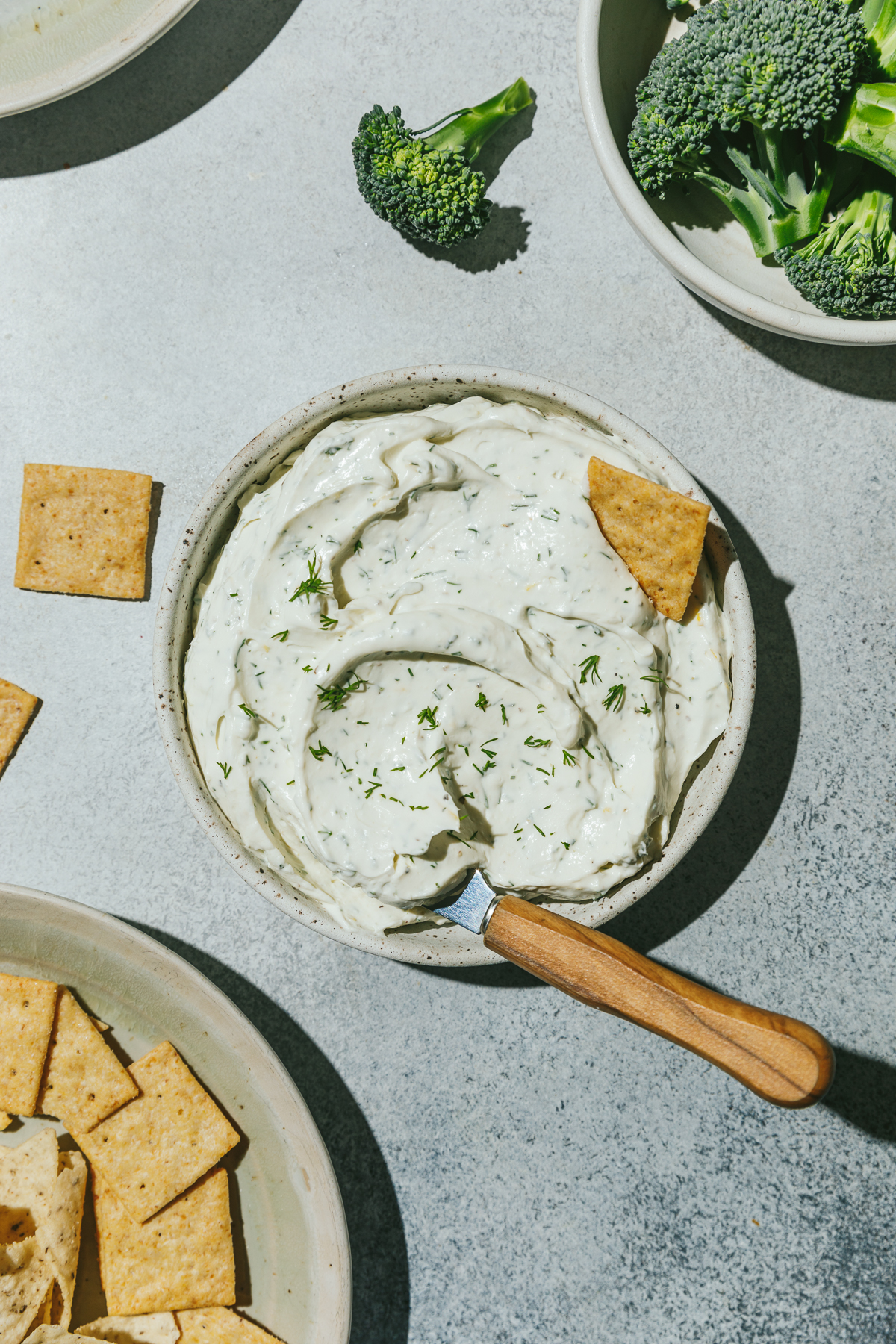 Dill cream cheese spread in a bowl with a bowl of crackers and broccoli.