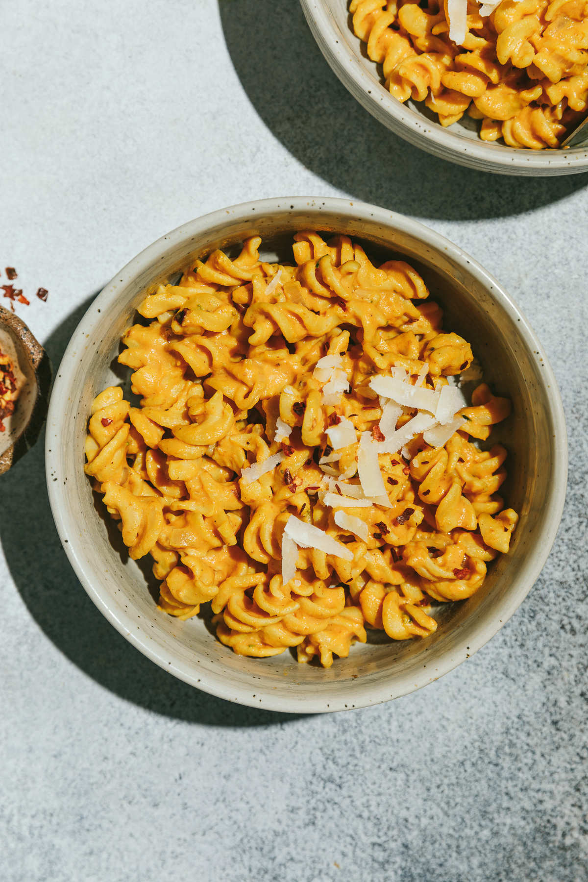 Two bowls of healthy pumpkin pasta on a gray surface.