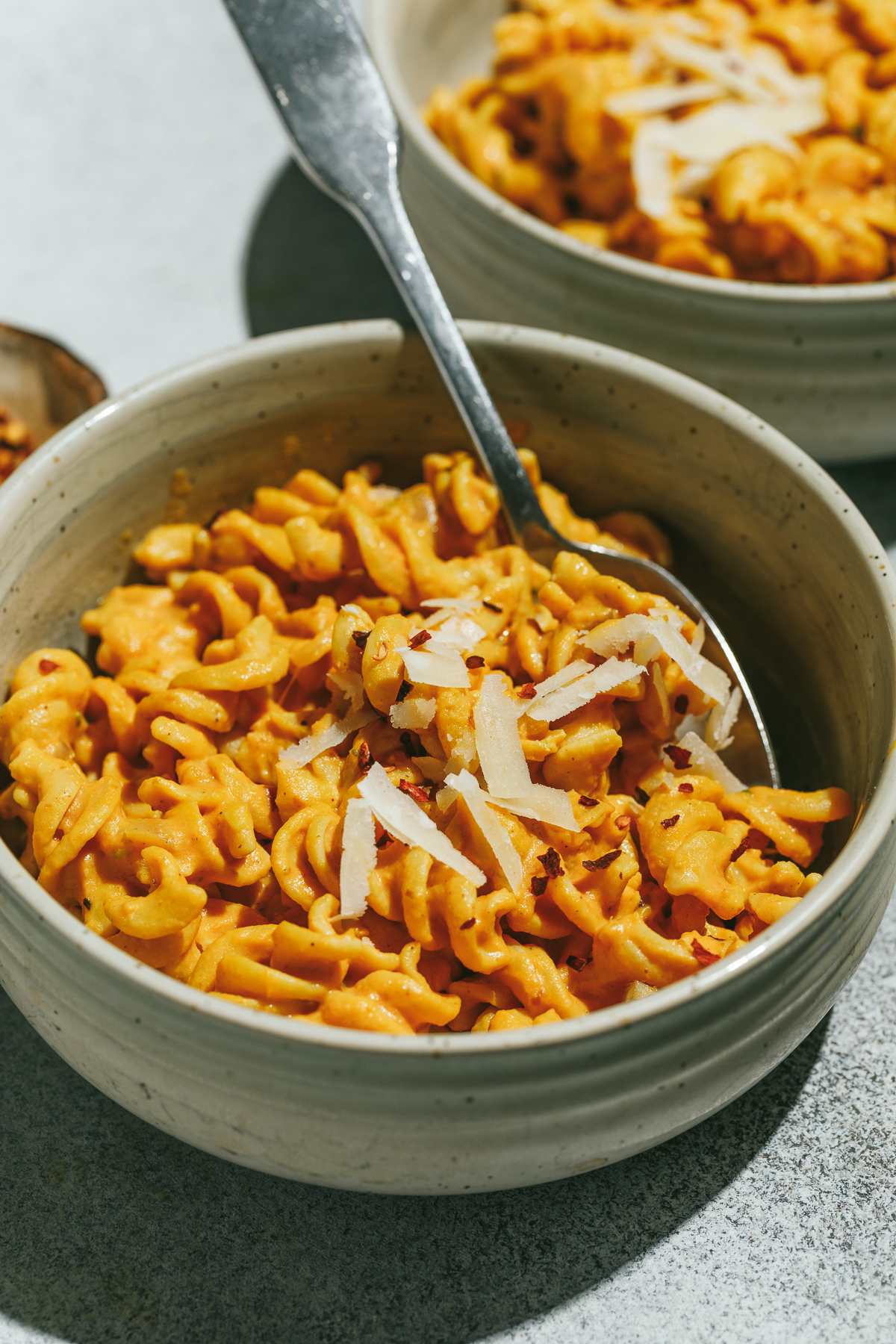 A bowl of healthy pumpkin pasta with a spoon and grated parmesan.
