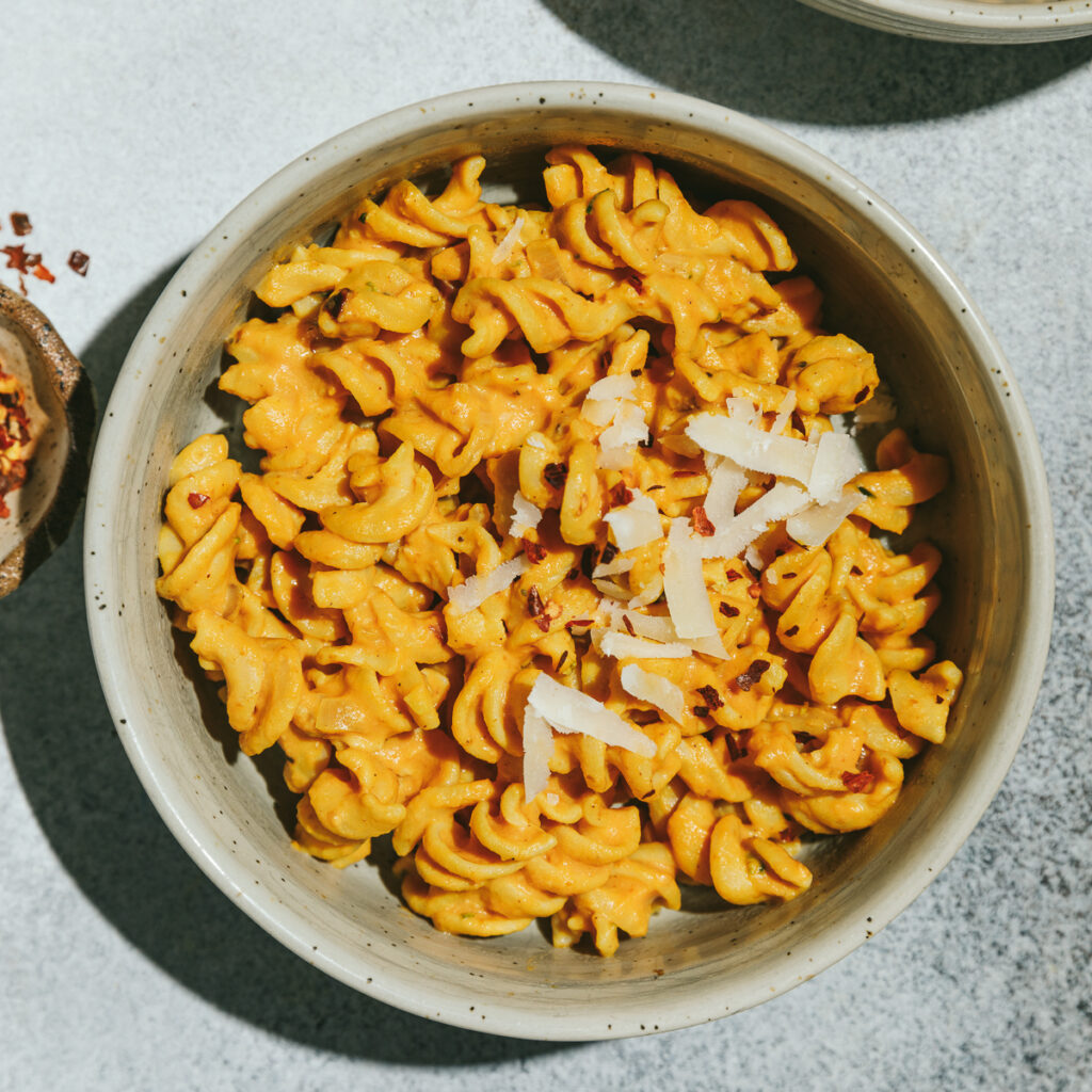 A bowl of healthy pumpkin pasta with grated Parmesan and chili flakes.
